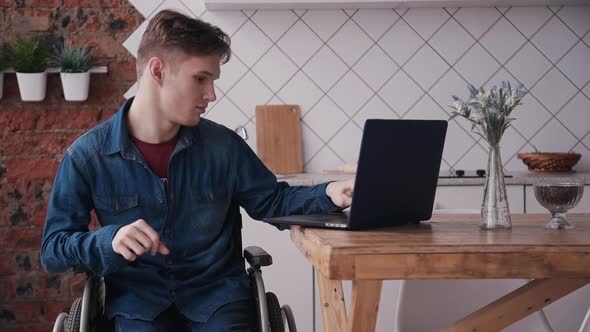 Adult Man in Wheelchair Using Personal Laptop and Sitting at Hom