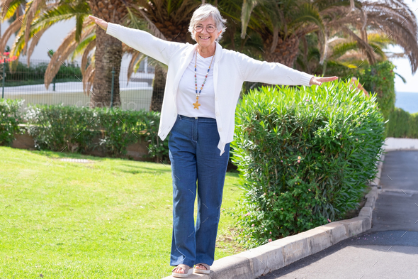 Happy senior woman walks on the curb with her arms outstretched to keep balance