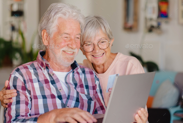 Portrait of happy modern elderly couple browsing together on laptop for shopping online