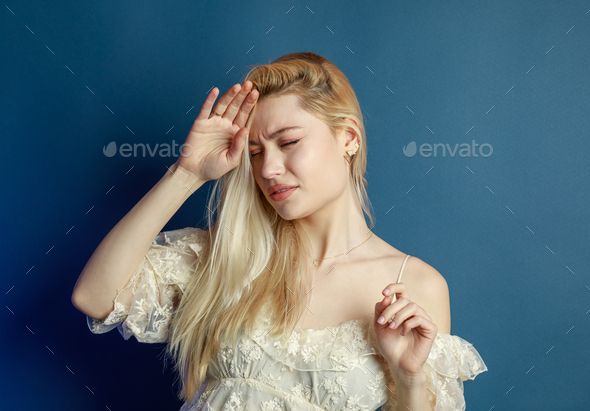 Beautiful lady feeling bad and put her hand to her forehead on blue background