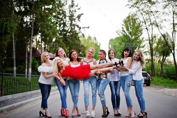 Crazy company of bridesmaids holding bride in red dress in the park at bachelorette party.