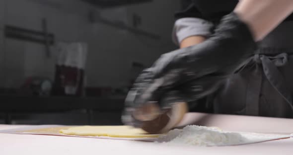 Closeup of a Baker's or Chef's Hand Rolling Out Dough on a White Table with Flour so That It Doesn't