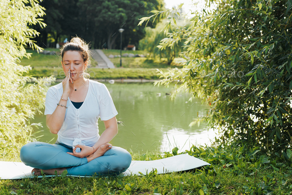 Young woman yogi meditating by the lake doing yoga asana nadi shodhana ...