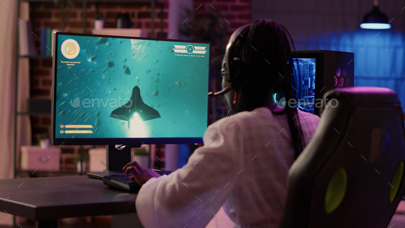 Over shoulder view of african american gamer girl playing space shooter simulation using pc gaming