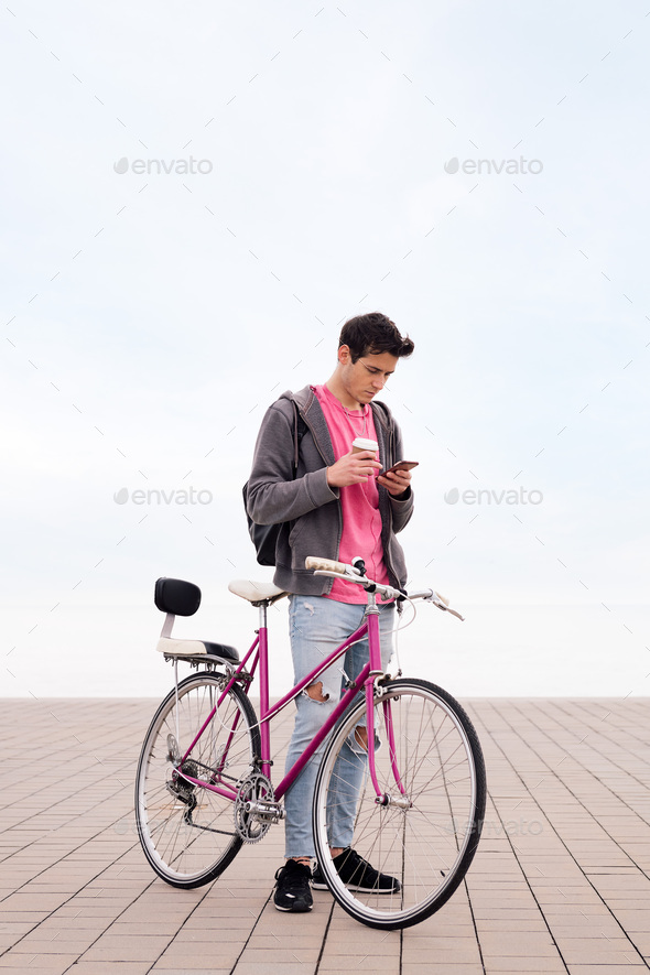 young man with bicycle and coffee using phone