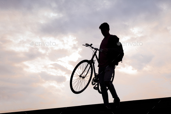 silhouette of a young man carrying bike down the stairs