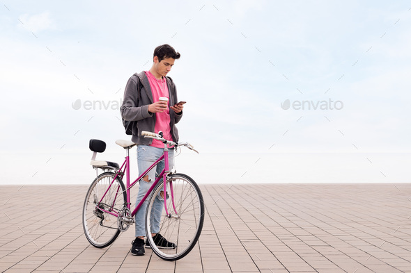 young man with bicycle and coffee looking phone