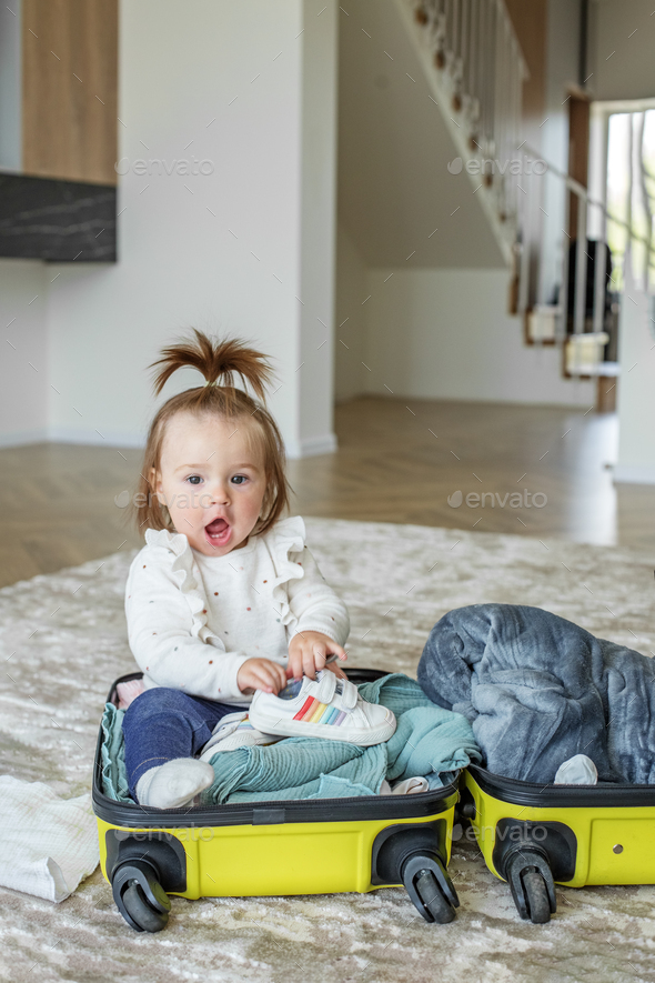 Happy little girl toddler tourist packs clothes in suitcase for travel, vacation