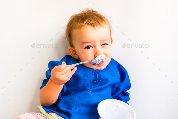 Baby savoring his first yogurt with a spoon, with a spotted face and adorable expression.
