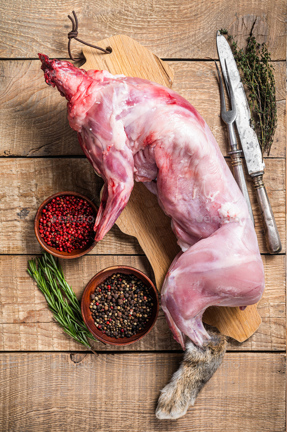 Raw Whole wild hare, fresh game meat on wooden board with herb. Wooden background. Top view