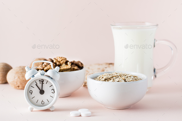 Foods for good sleep - milk, walnuts, oatmeal, sleping pill and alarm clock on pink background