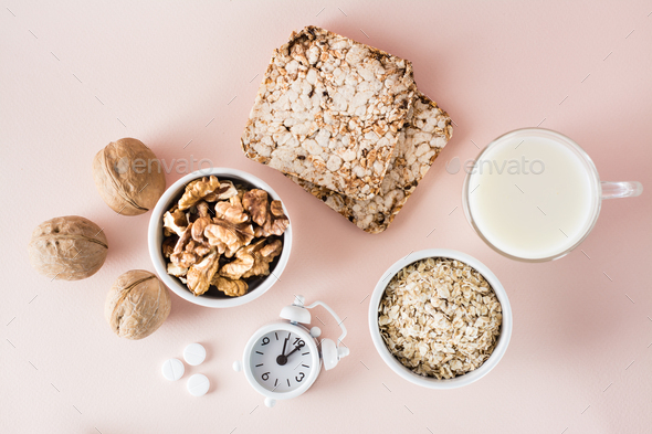 Foods for good sleep - milk, walnuts, crispbread, oatmeal, sleeping pill and alarm clock on pink