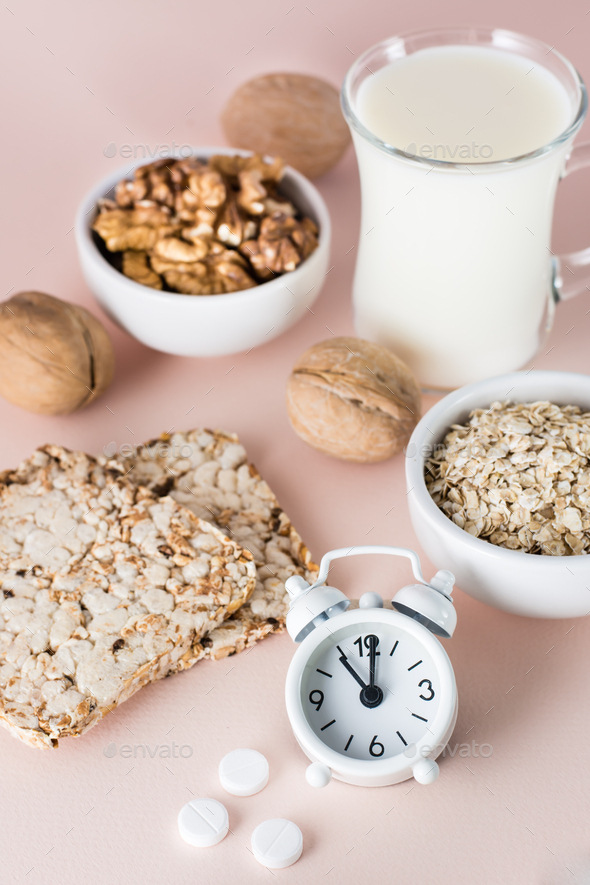 Foods for good sleep - milk, walnuts, crispbread, oatmeal, sleeping pill and alarm clock on pink