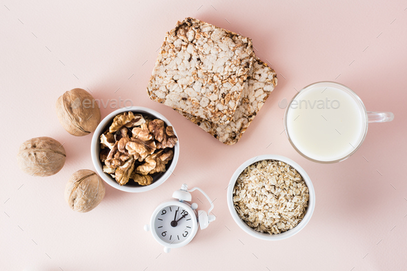 Foods for good sleep - milk, walnuts, crispbread, oatmeal and alarm clock on pink background.