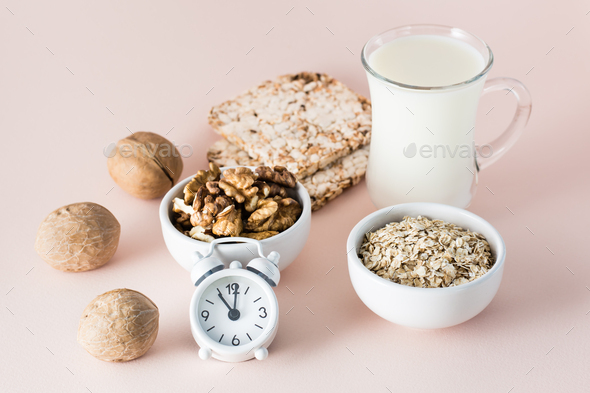 Foods for good sleep - milk, walnuts, crispbread, oatmeal and alarm clock on pink background