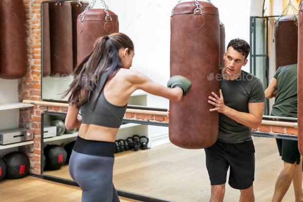 Sportswoman in boxing gloves training with instructor in gym