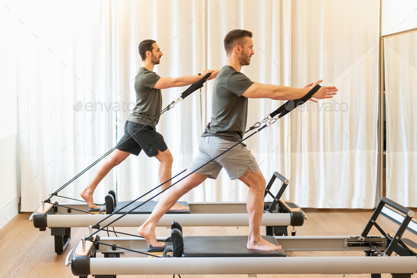 Fit men exercising on pilates machines in gym
