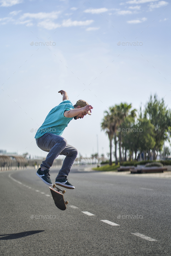 a man doing an ollie flip with his skateboard down a road