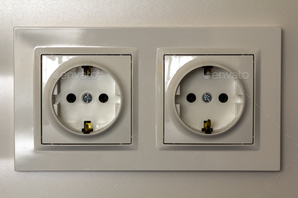 New white shiny plastic electric double sockets on white wall background. Advantages and comfort of