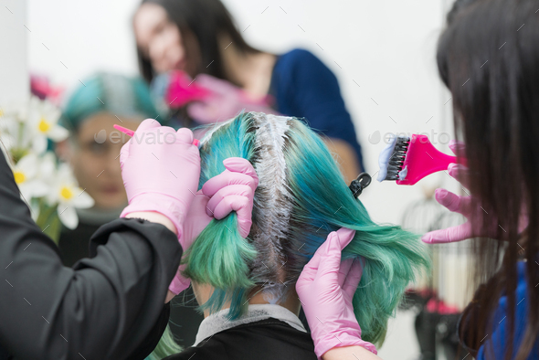 Process of hair dyeing in salon. Two hairdressers applying paint to hair during bleaching hair roots