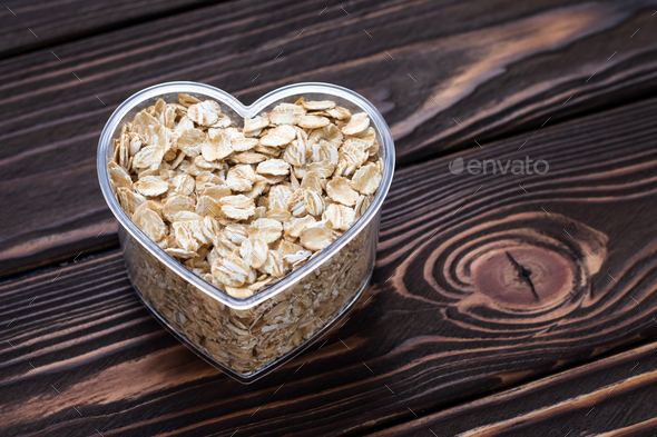 One heart of oat-flakes, uncooked oats on brown wooden board background.