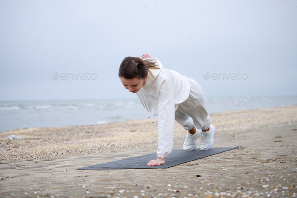The young beautiful girl laying on the yoga mat and doing one arm push ups