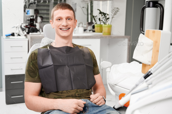 Young man with dental braces at dentist office sitting in dentist chair