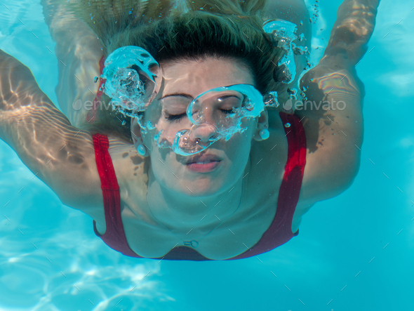 Blonde girl diving in the pool and breathing out air to make bubbles.