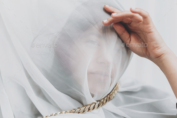 Beautiful woman under veil posing with golden necklace in room. Self care. Social isolation