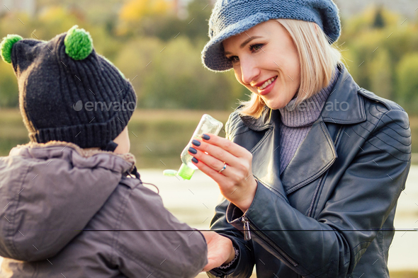 Mother in a warm jacket and knitted hat apply an antiseptic gel antibacterial gel