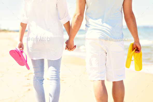 Couple walking at the beach and carrying flip flops