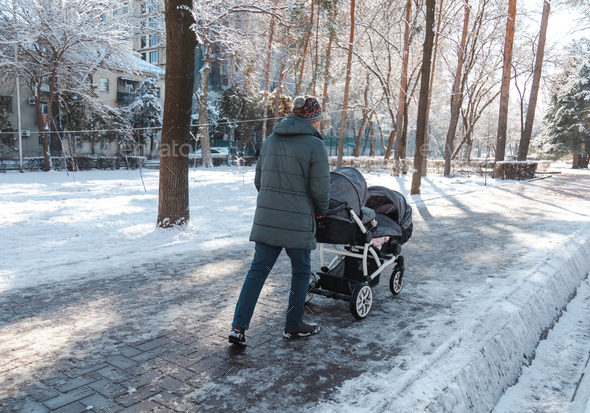 Father pushing a baby stroller for twins walking outside in winter