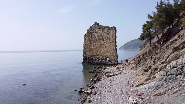An unusual rock standing in the sea. Flat rock in the form of a sail with a hole in the middle