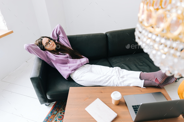 Young caucasian woman relaxing on a sofa in front laptop in living room after work.