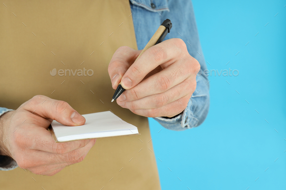 Male waiter writes order on blue background