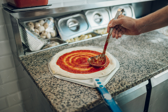 Man worker in a pizza place placing ingredients on pizza dough