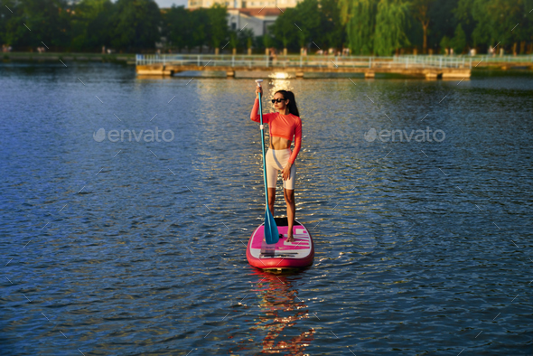 Athletic woman practising in sup surfing during sunset