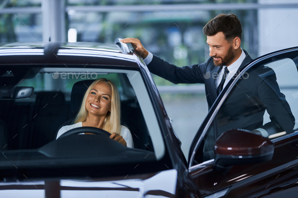 Salesman showing to female customer various auto at salon