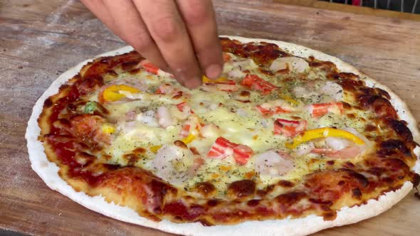 hands sprinkle oregano and sauce on charcoal pizza homemade