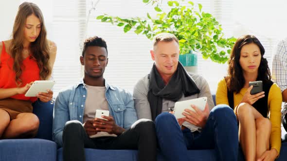 Business colleagues using electronic devices while sitting on sofa alt
