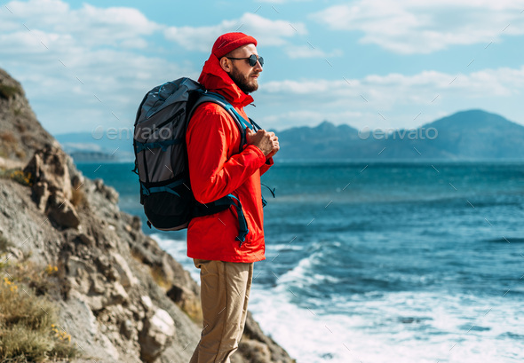 A tourist with a backpack on his back stands against the backdrop of a beautiful seascape - Stock Photo - Images