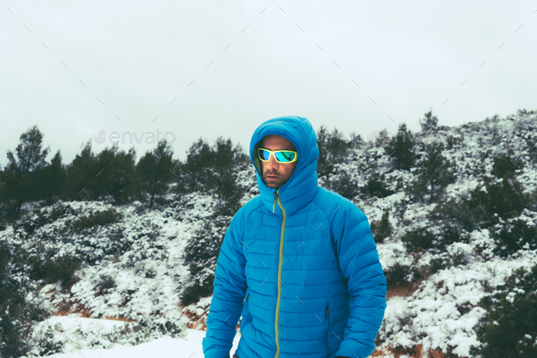 Hiker walks down the mountain during a snow covered in a down coat.