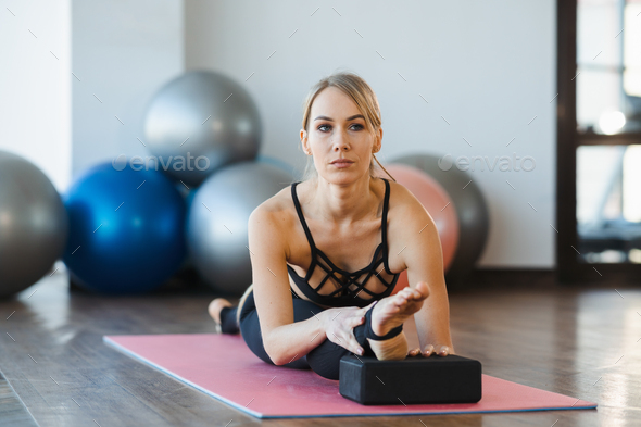 Beautiful fitness girl sitting on a twine with blocks for stretching indoors
