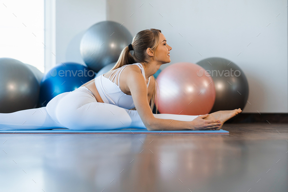 Flexible girl in white yoga clothes practicing twine in fitness studio
