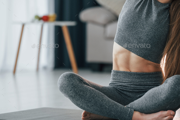Strong abs. Young woman with slim body type and in yoga clothes is at home  Stock Photo by mstandret