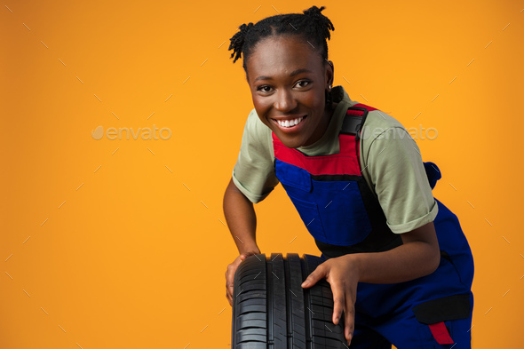 Portrait of smiling black female mechanic posing with new car tyres in studio