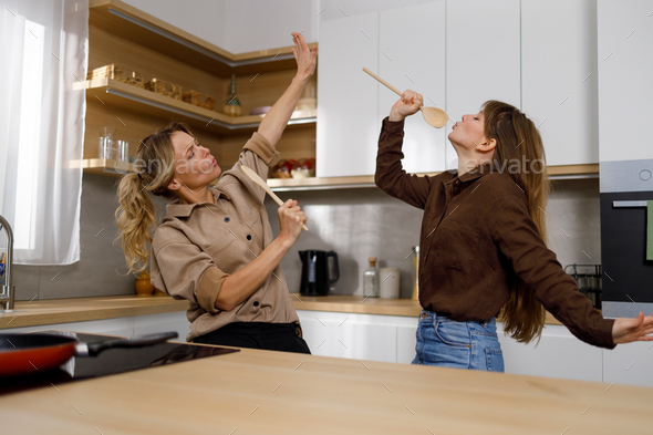 Two women sing and dancing in the kitchen at home