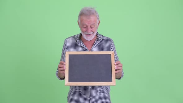 Happy Senior Bearded Man Holding Blackboard and Looking Surprised alt