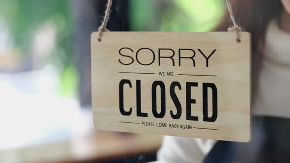 The business owner is walking to close the sign hanging in the shop to close customer service. alt