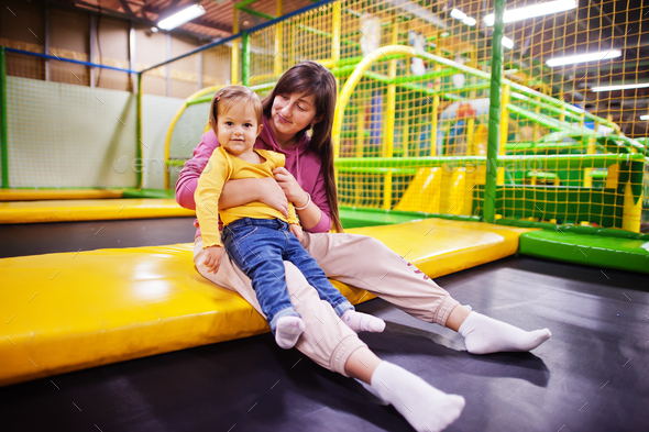 Mother with daughter sitting on a trampoline in indoor play center.